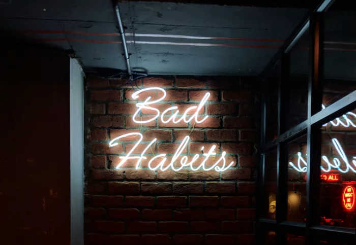 Bad Habits neon sign hanging on a brick wall