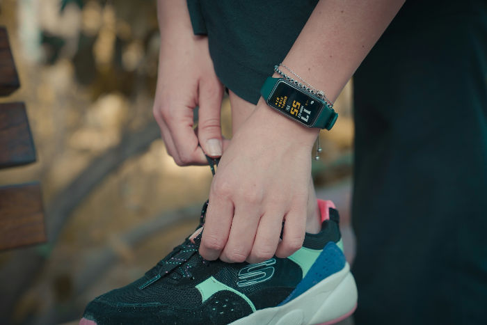 Woman kneeling to tie shoe lace wearing a fitness tracker 