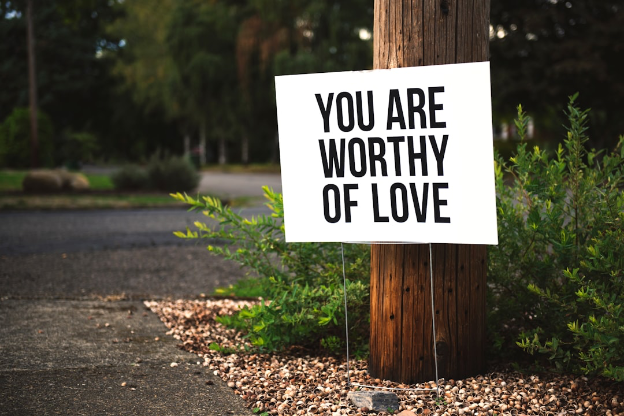 A “You are worthy of love” sign on the ground in front of a telephone pole