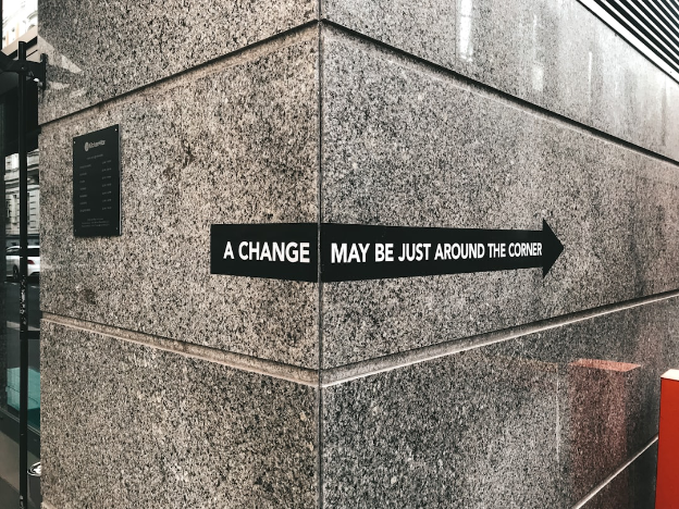 Sign says “a change may be just around the corner” posted on a corner wall with an arrow