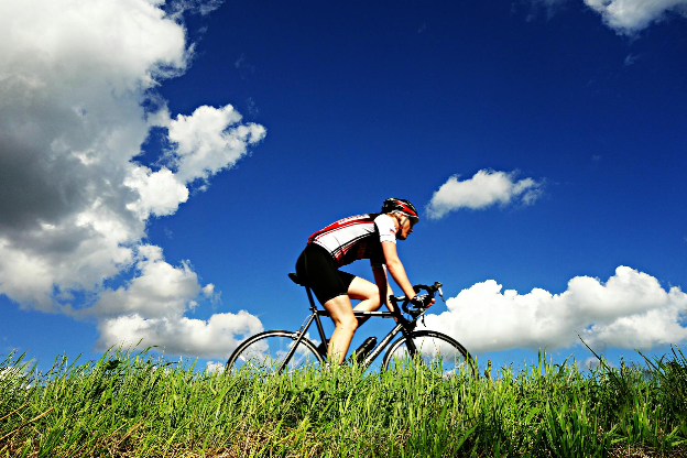 Person riding a bicycle with blue sky and white clouds in the background