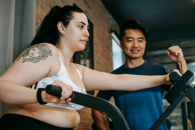 Young man helping an older woman on the elliptical machine