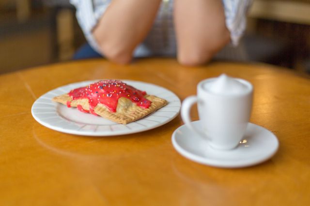 Pop-tart on plate with coffee cup on wooden table, hands folded