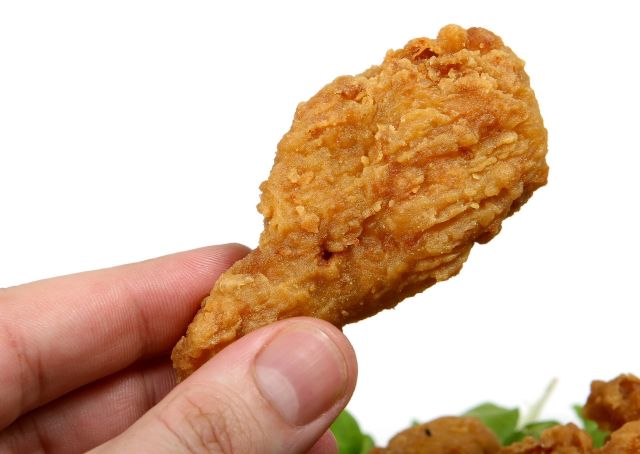 Hand Holding Fried Chicken Nugget Over Pile of Lettuce